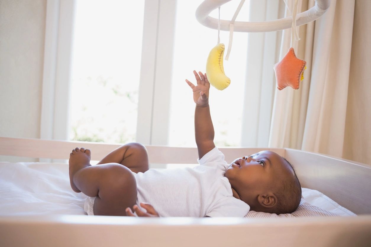 A baby laying in bed under a mobile.