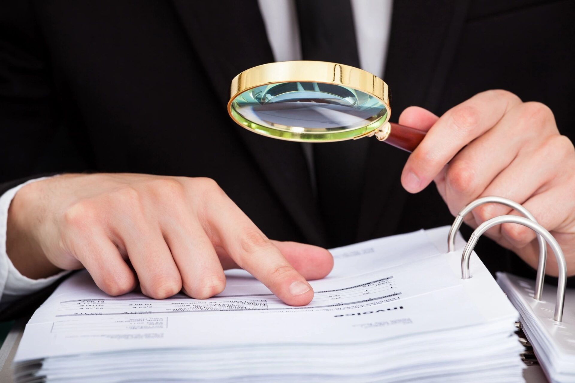 A person holding a magnifying glass over papers.