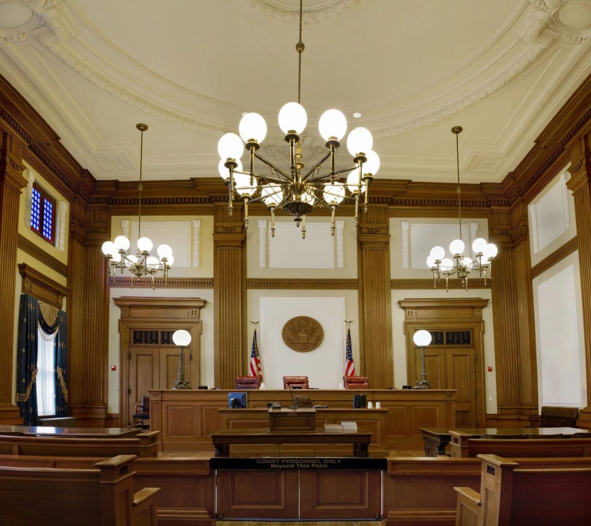 A courtroom with many wooden benches and chandeliers.