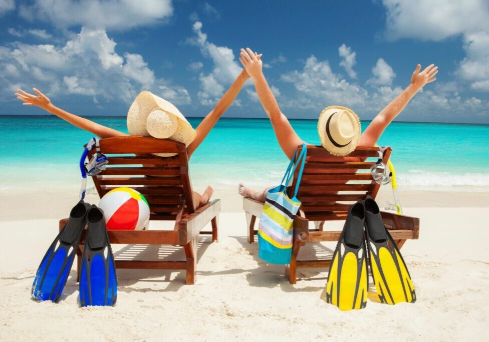 Two people sitting on a beach with their arms up.