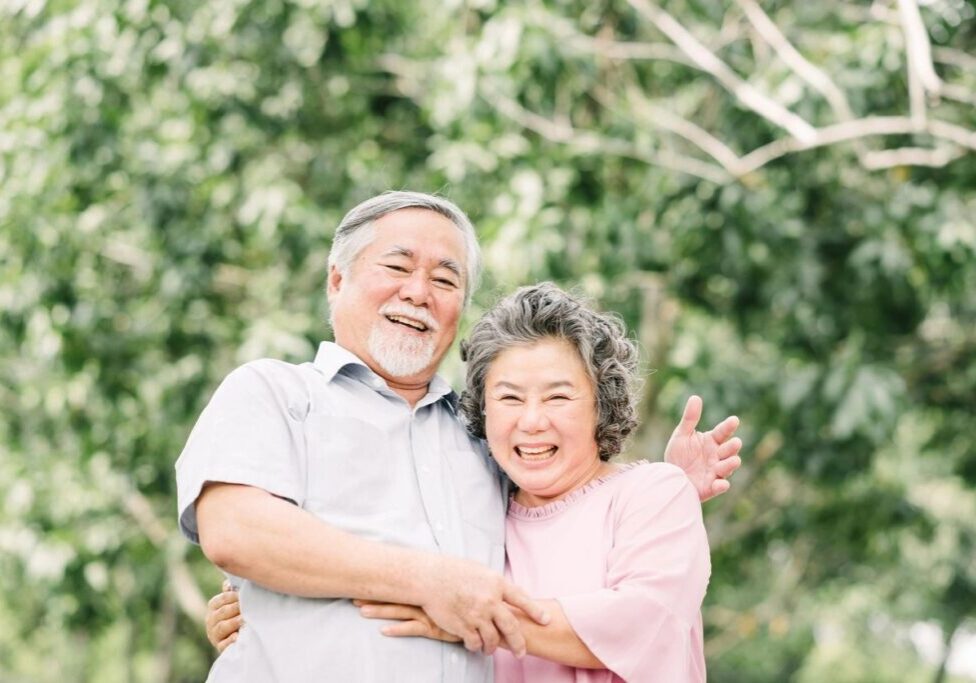 An older couple posing for a picture in front of trees.