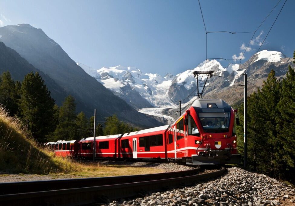 A train is traveling down the tracks near some mountains.