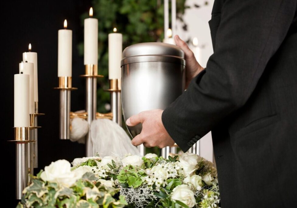 A person holding a urn in front of flowers.