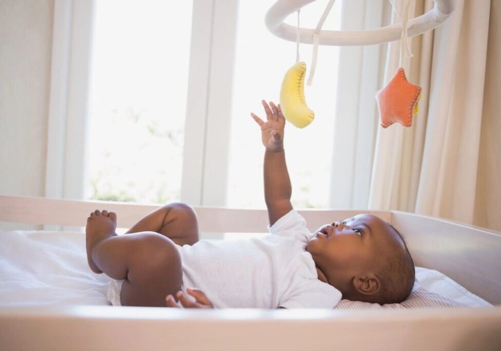 A baby laying in bed under a mobile.