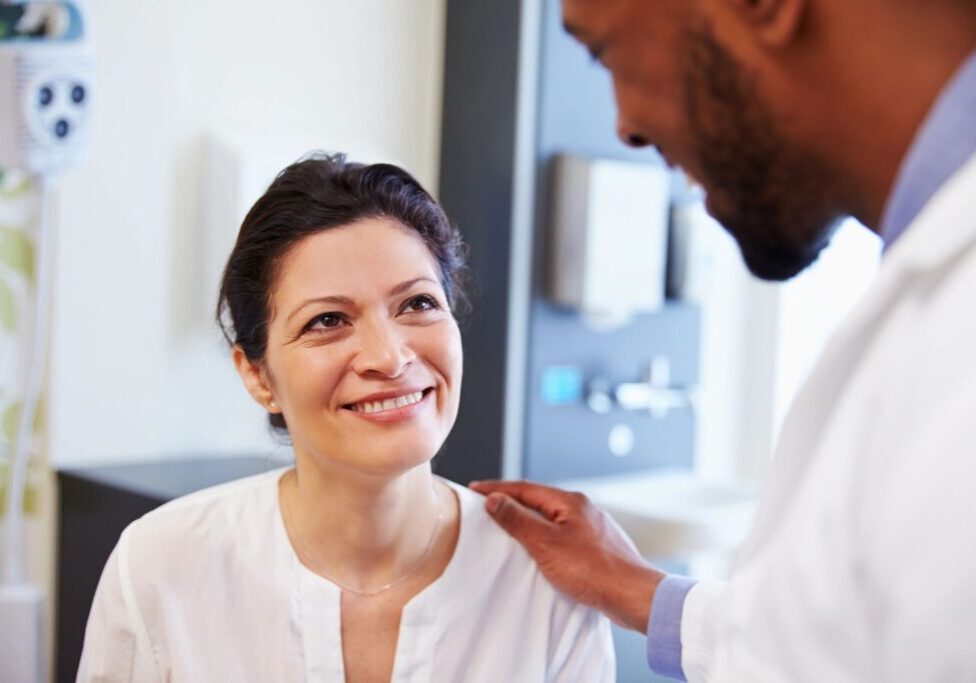 A woman smiling at the camera while being examined by a doctor.